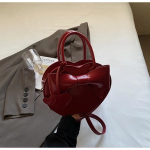 Détail du sac à main rouge en forme de cœur avec un grand nœud et aspect cuir brillant
