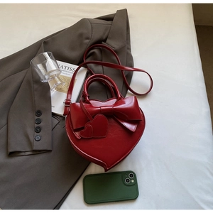 Détail du sac à main rouge en forme de cœur avec un grand nœud et des charms