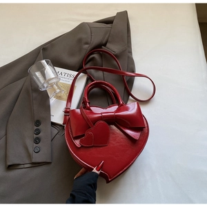 Vue détaillée d'un sac à main rouge en forme de cœur avec nœud et breloques de cœur