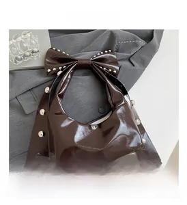 Detail of studded bow handle on dark brown glossy faux leather shoulder bag