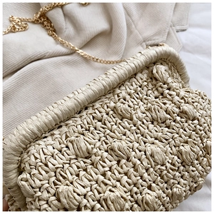 Close-up of the beige woven texture and golden chain on this artisanal straw bag