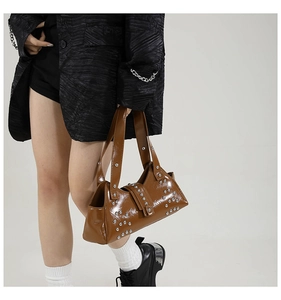 Détail d'un sac à main marron en cuir verni avec des rivets argentés au style punk