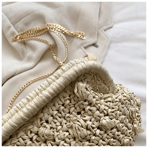 Detail of hand-woven beige clutch texture with shiny gold chain strap and soft fabric background