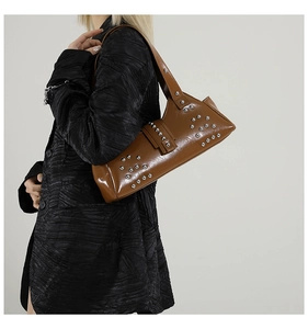 Détail d'un sac baguette en cuir marron à clous argentés porté avec un blazer noir chic
