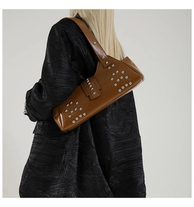 Détail de rivets argentés sur un sac à bandoulière en cuir marron brillant style punk