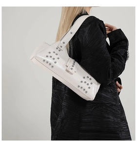 Détail d'un sac à bandoulière en cuir blanc avec des clous argentés porté par un mannequin