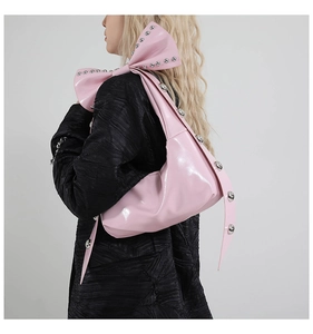 Detail of pink patent leather tote with oversized rivet bow strap on model side view