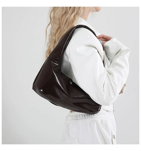 Nahaufnahme einer dunkelbraunen Lackleder-Hobo-Tasche mit Hochglanz-Finish an der Schulter