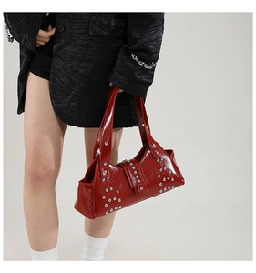 Détail du sac à main en cuir verni rouge avec rivets punk argentés et bandoulière large