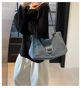 Detail of blue denim shoulder bag with silver metal buckle and chain strap on a model