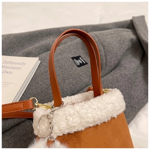Detail of suede bucket bag with white faux fur trim and plush pom-pom accessory