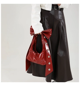 Detail of red patent leather shoulder bag with oversized bow and silver metal rivets