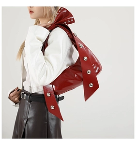 Detail of red patent leather shoulder bag with silver studs and bow-shaped strap design