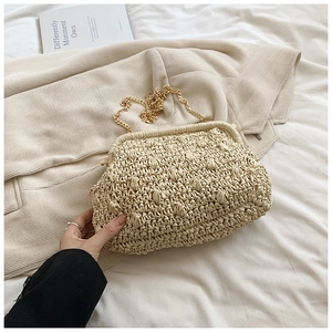 Detail of beige woven straw clutch with wave pattern, gold chain strap and metal clasp