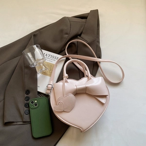Sac à main rose en forme de cœur avec grand nœud et bandoulière sur un blazer brun