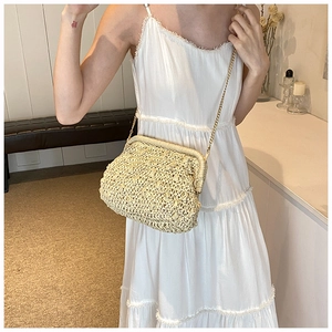 Detail of handmade straw clutch with gold chain strap worn over a white lace dress