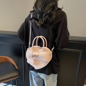 Sac à main rose en forme de cœur avec nœud et bandoulière porté sur un sweat à capuche