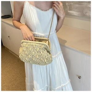 Detail of beige straw clutch with golden chain strap and woven texture on model