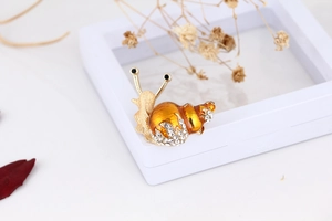 Close-up of a snail brooch with orange enamel shell and sparkling rhinestone details