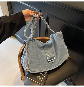 Detail of washed blue denim tote featuring silver metal chain and vintage buckle closure