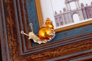 Detail view of a snail brooch with orange enamel shell and sparkling white rhinestones