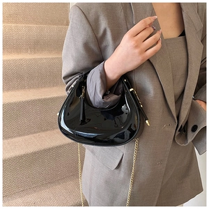 Détail du sac hobo en cuir verni noir brillant avec chaîne dorée et breloque à pompon