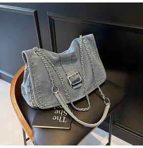 Detail of light blue denim tote bag with silver metal buckle and chain strap