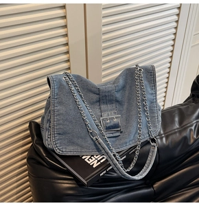 Detail of blue denim shoulder bag featuring a large silver buckle and chain strap