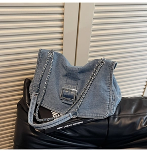 Detail of blue denim shoulder bag with silver chain strap and large metal buckle