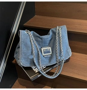 Detail of blue denim tote bag featuring silver square buckle and chain shoulder strap