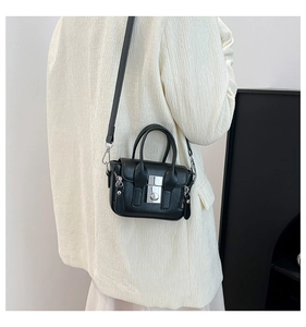 Détail d'un mini sac noir à bandoulière avec boucle argentée sur un blazer blanc
