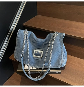 Close-up of blue denim shoulder bag with silver buckle and chain strap on wooden stairs