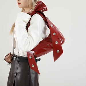 Red glossy shoulder bag with silver rivet studs and bow strap on model side view