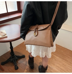 Brown leather crossbody bag detail with golden horseshoe buckle on a stylish model