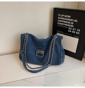 Detail of blue denim tote bag with silver chain strap and large metal buckle on marble