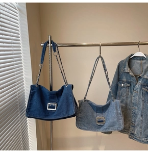 Detail of blue denim tote bags with metal buckles and chain straps hanging on a rack