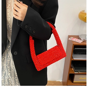 Macro detail of red handcrafted beaded underarm bag showing woven texture on a dark suit