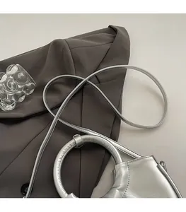 Détail du sac en cuir argenté avec poignée ronde et bandoulière fine sur un fond chic