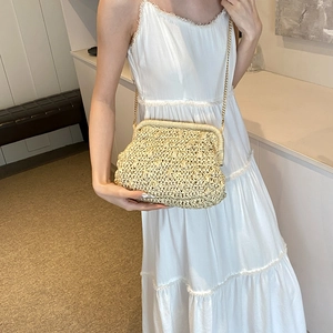 Handmade woven straw clutch bag with gold chain strap shown on a white dress model