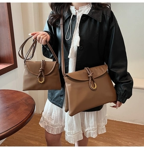 Detail of woven leather handle and gold horseshoe buckle on dark brown crossbody bag