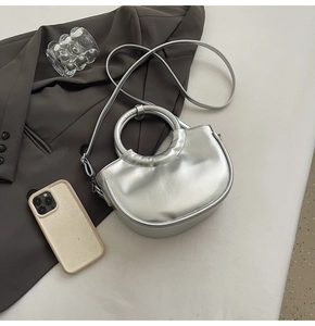 Detail of silver metallic crescent bag with circular handle and detachable shoulder strap