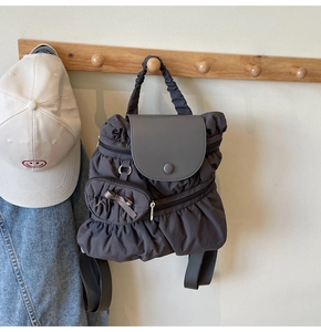 Detail of grey pleated nylon backpack with a bow accessory hanging on a wooden hook