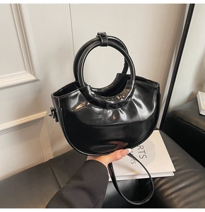 Detailed view of black patent leather crescent bag with circular handle and thin shoulder strap