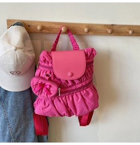 Detail of pink pleated nylon backpack with matching heart shaped charm hanging on a rack