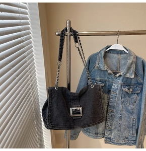 Detail of dark grey washed denim tote with silver metal buckle and chain strap on a hanger