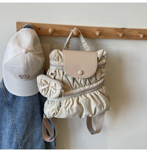 Detail of beige pleated nylon backpack with heart-shaped pendant on wooden hanger