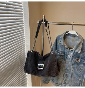 Detail of black washed denim shoulder bag featuring silver chain strap and oversized buckle