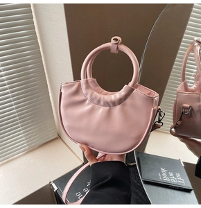 Detailed view of pink semi-circular handbag with circular handle and detachable strap