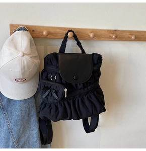 Detail of black pleated nylon backpack with leather flap and mini bow purse charm