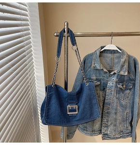Detail of dark blue denim shoulder bag featuring silver buckle and chain strap on a hanger